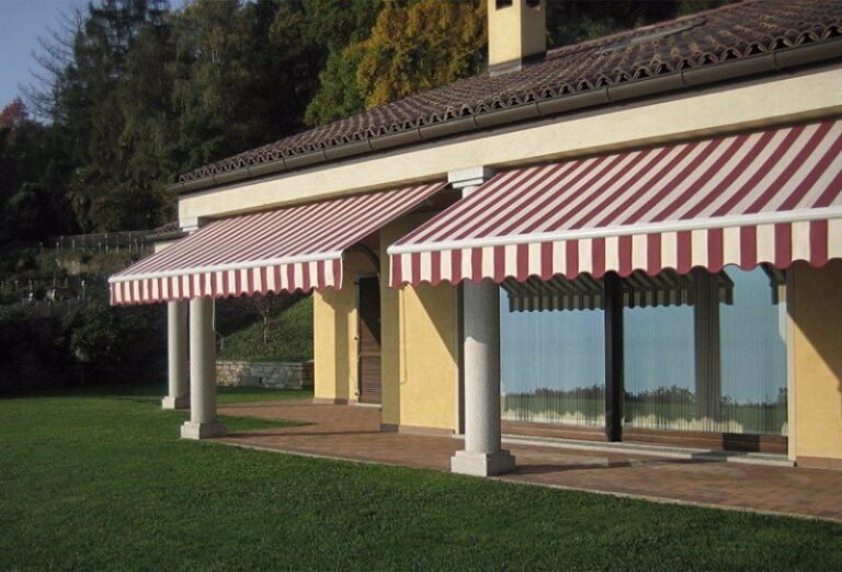 Due tende da sole a bracci in tessuto a righe rosse e bianche montate sulla facciata di una casa