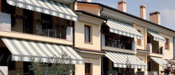 Tende da sole in tessuto chiaro installate sui balconi di una palazzina residenziale